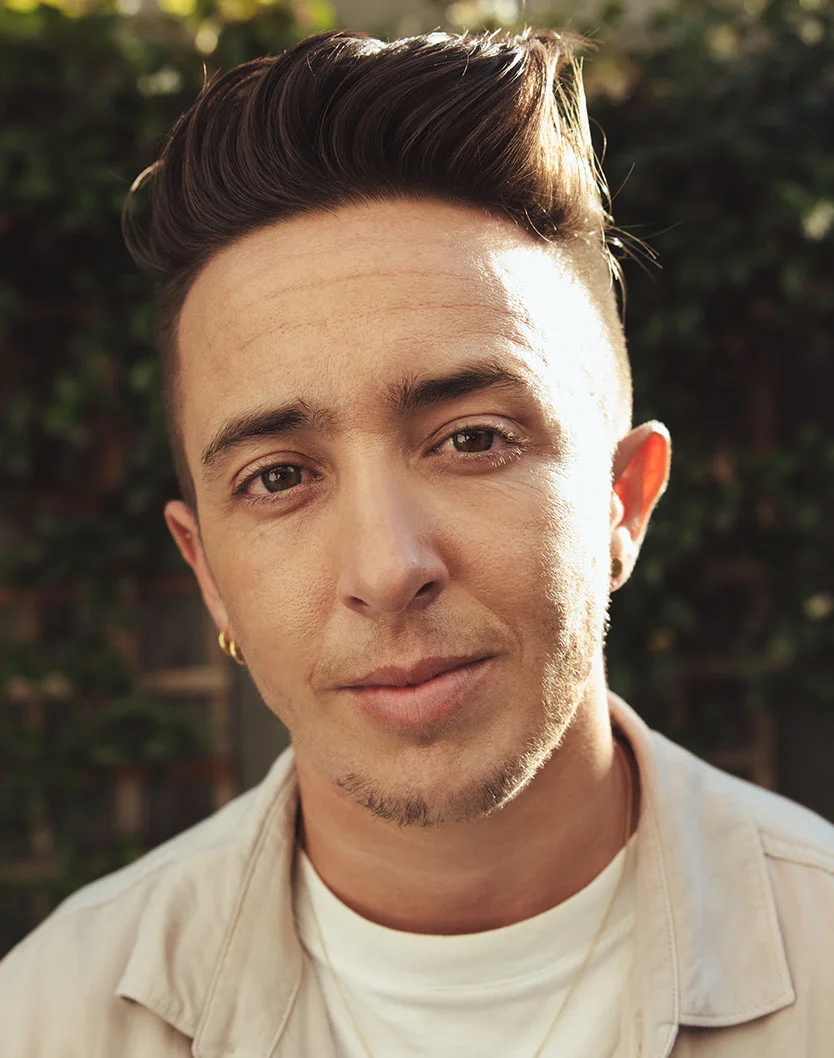 Close-up outdoor portrait of a young person with a stylish dark haircut and a light-colored shirt, smiling subtly at the camera. - GA Chin Implants in San Fransisco, CA