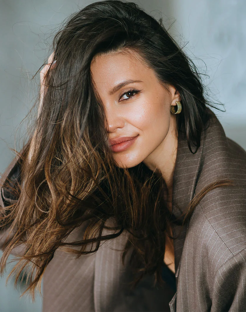 A beautiful young woman with long, dark, wavy hair covering part of her face, looking directly at the camera, potentially illustrating the result or desired outcome of a cosmetic procedure like hairline lowering or laser hair removal. - Hairline Lowering in San Fransisco, CA