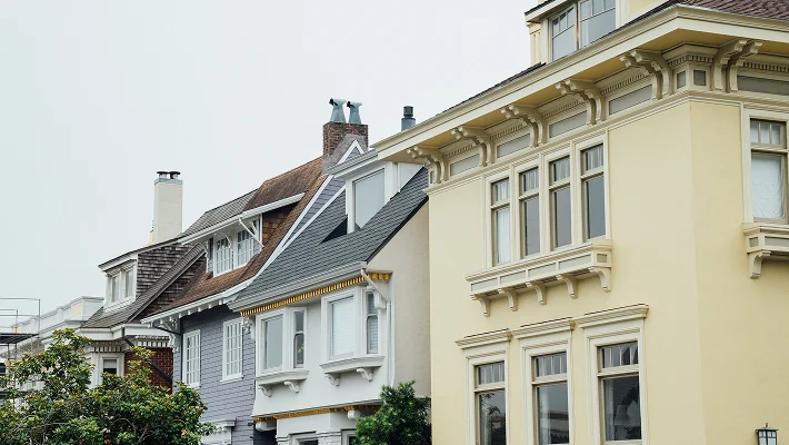 A row of light-colored, ornate Victorian-style townhouses with varying rooflines and architectural details.